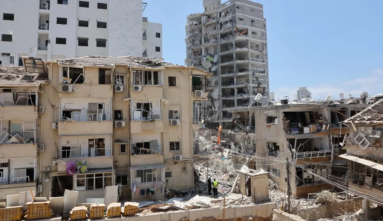 Petugas tanggap darurat Israel berdiri di antara puing-puing bangunan yang rusak berat, setelah serangan rudal Iran semalam di Bat Yam pada 15 Juni 2025. (GIL COHEN-MAGEN/AFP)