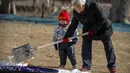 Seorang anak menyaksikan orang dewasa menyekop salju di sebuah taman umum di Beijing, Selasa (17/1/2023). China telah mengumumkan penurunan populasi pertamanya dalam beberapa dasawarsa seiring bertambahnya usia negara terpadat di dunia dan angka kelahirannya yang menurun. (AP Photo/Mark Schiefelbein)