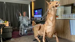 David Marriott berpose dengan kuda kertasnya Russell di kamar hotelnya di Brisbane, Australia, 6 April 2021. Saat berada dalam kamar hotel untuk karantina, direktur seni di iklan TV itu bosan dan mulai membuat pakaian koboi dari kantong kertas makanannya yang dikirimkan. (David Marriott via AP)