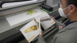 Wilson Tong, CEO LifeArt Asia, melihat katalog pilihan desain peti mati saat mesin sedang mencetak gambar Lily di sampul peti mati, di ong Kong, Jumat, 18 Maret 2022. Perusahaan itu mencoba membuat alternatif peti mati dari kardus yang diklaim ramah lingkungan. (AP Photo/Kin Cheung)