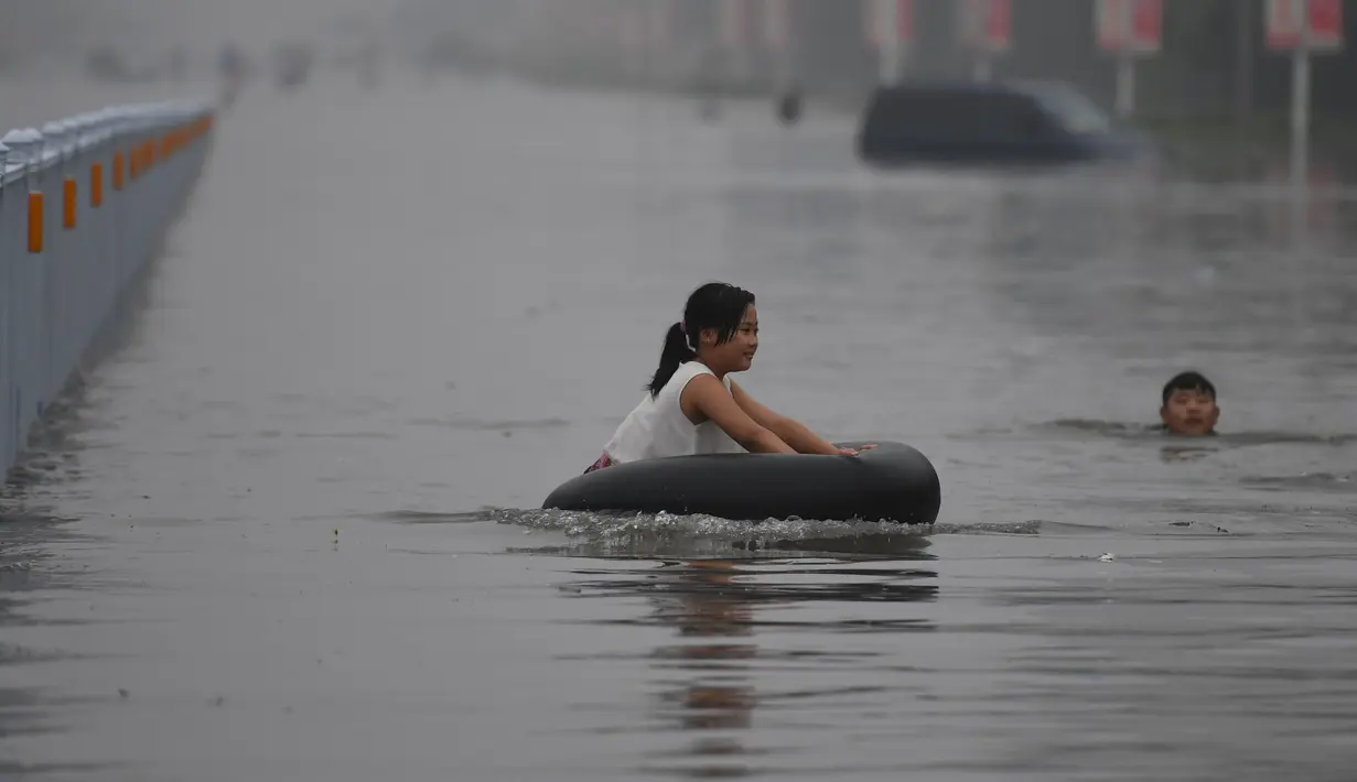 Seorang anak perempuan bermain ban saat banjir melanda Xinxiang, Provinsi Henan, Tiongkok, (9/7). Sedikitnya 420 ribu warga dari 4 kota setempat, termasuk ibukota Fuzhou terpaksa dievakuasi ke tempat yang lebih aman. (REUTERS)