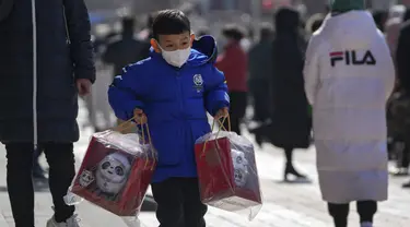 Seorang anak membawa boneka maskot Olimpiade Bing Dwen Dwen melewati warga yang berbaris di luar toko yang menjual memorabilia resmi Olimpiade di Beijing, 21 Februari 2022. Boneka maskot Olimpiade masih tetap populer meskipun Olimpiade Musim Dingin Beijing telah berakhir. (AP Photo/Andy Wong)