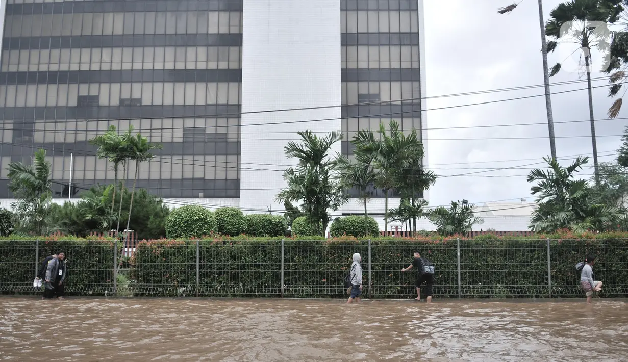 Warga pengguna transportasi umum berjalan kaki melintasi banjir di Jalan Ahmad Yani, Jakarta, Minggu (23/2/2020). Pengguna transportasi umum seperti Transjakarta dan ojek online terpaksa berjalan kaki akibat kendaraan yang mereka tumpangi tidak bisa melintasi banjir. (merdeka.com/Iqbal S. Nugroho)