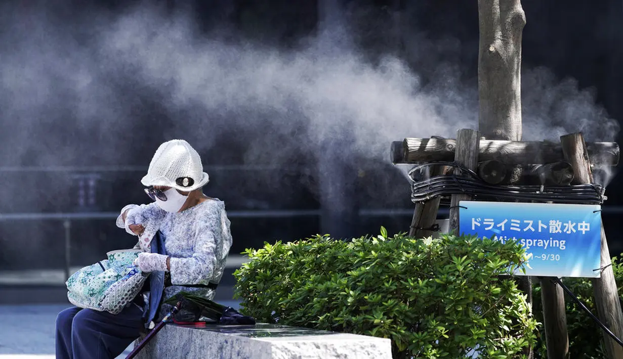 Seorang wanita mengenakan masker untuk mencegah penyebaran Covid-19 di bawah titik kabut dingin di Tokyo (12/8/2020). Menurut Badan Meteorologi Jepang, cuaca panas telah ditetapkan dengan suhu naik lebih dari 34 derajat Celcius (93,2 derajat Fahrenheit) di Tokyo. (AP Photo/Eugene Hoshiko)