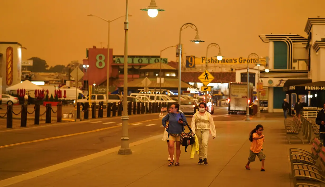 Sejumlah orang berjalan saat kabut asap menyelimuti langit di Fisherman's Wharf, San Francisco, Amerika Serikat, Rabu (9/9/2020). Kebakaran hutan di seluruh Barat mengakibatkan langit San Francisco hingga Seattle berwarna oranye yang menakutkan. (AP Photo/Eric Risberg)