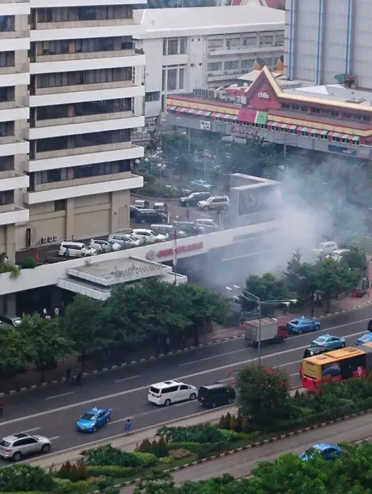Asap terlihat membumbung di sekitar pos polisi Lalu Lintas di Jalan HM Thamrin, Jakarta, pasca ledakan, Kamis (14/1). Sedangkan di luar pos, terdapat tiga orang tergeletak dengan darah berceceran. (twitter.com/ReesEdward) 
