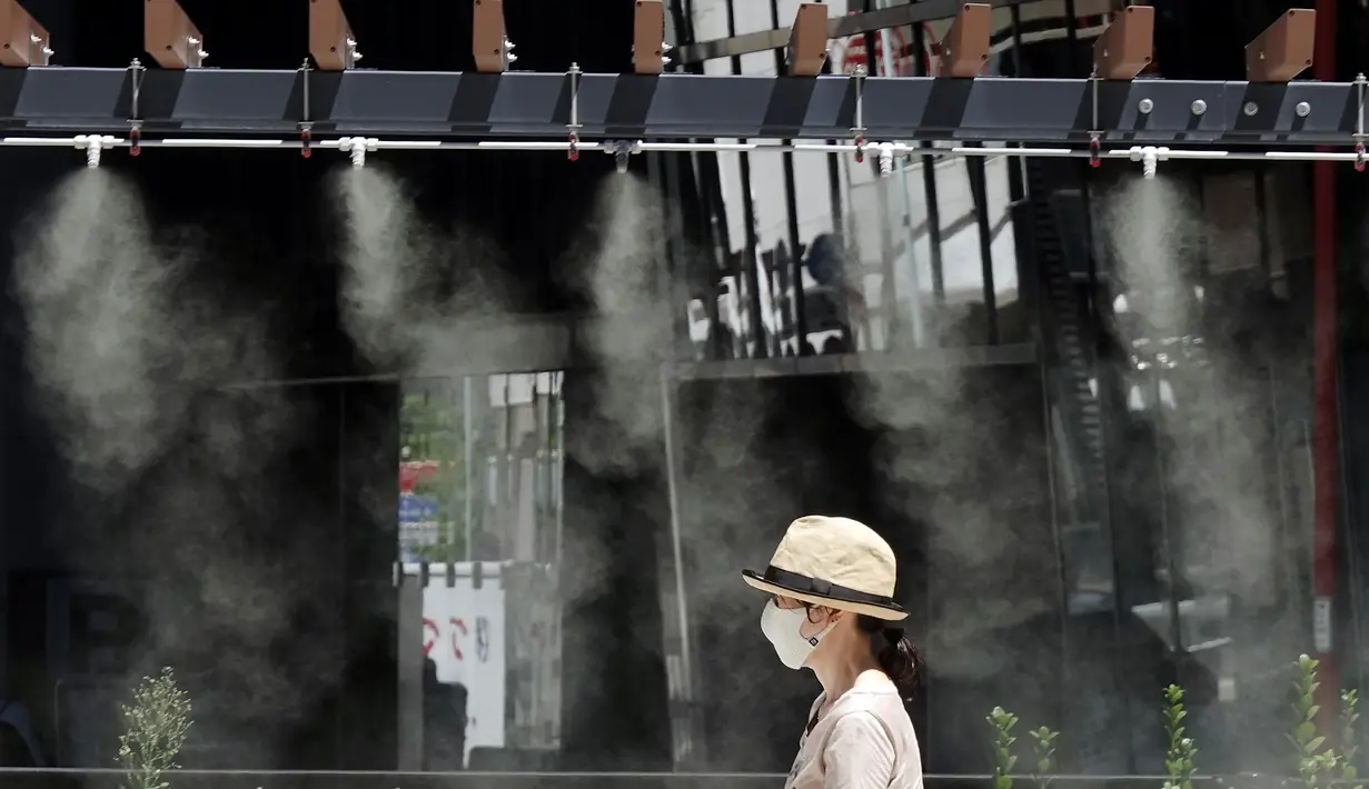 Seorang wanita berjalan di bawah titik kabut yang menyejukkan di sepanjang jalan di Tokyo, Selasa (10/8/2021). Menurut biro meteorologi Jepang, cuaca panas panas terus berlanjut di wilayah metropolitan saat suhu naik menjadi 338 derajat Celcius (100,4 derajat Fahrenheit). (AP Photo/Eugene Hoshiko)