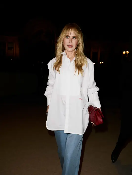 Nicole Kidman bergaya semi formal dengan kemeja putih oversized dan trouser biru denim. Tas Chanel merah gelap jadi aksesori kontras yang dijinjingnya [Chanel]