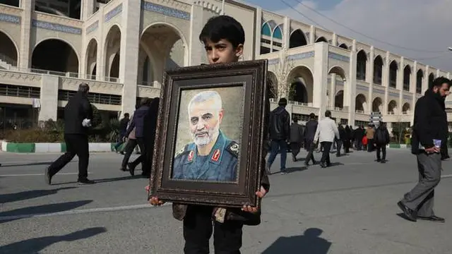 Seorang bocah laki-laki memegang foto Qasem Soleimani dalam acara pemakamannya.