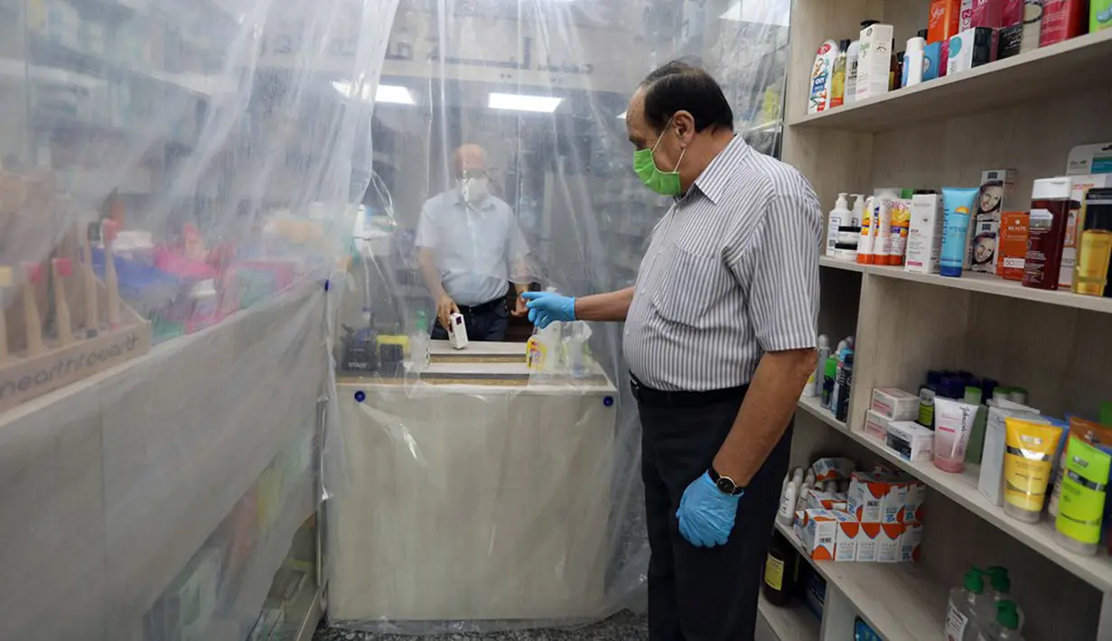 Lapisan plastik digunakan untuk mengurangi kontak fisik antara pegawai dengan pembeli di sebuah apotek di Baghdad, Irak, Selasa (14/4/2020). Menjaga jarak fisik atau physical distancing dinilai langkah paling tepat untuk mengurangi penyebaran virus corona COVID-19. (Xinhua)