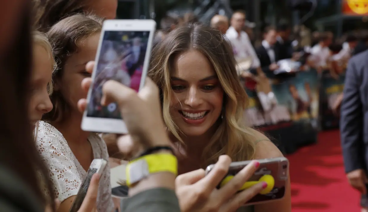 Aktris Margot Robbie berselfie dengan penggemar saat tiba menghadiri pemutaran perdana film 'Once Upon A Time in Hollywood' di Berlin, Jerman (1/8/2019). Margot Robbie tampil cantik mengenakan gaun hijau zaitun dari koleksi Jacquemus's Spring 2020. (AFP Photo/Odd Andersen)