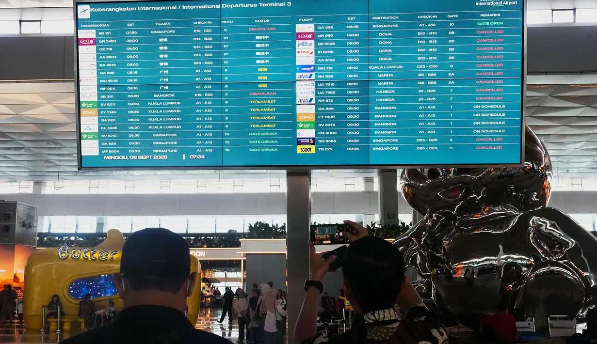 Calon penumpang berjalan melewati papan informasi yang menunjukkan penerbangan terganggu di Bandara Internasional Soekarno-Hatta di Tangerang, Indonesia, Minggu, 6 September 2026. (AP Photo/Tatan Syuflana)
