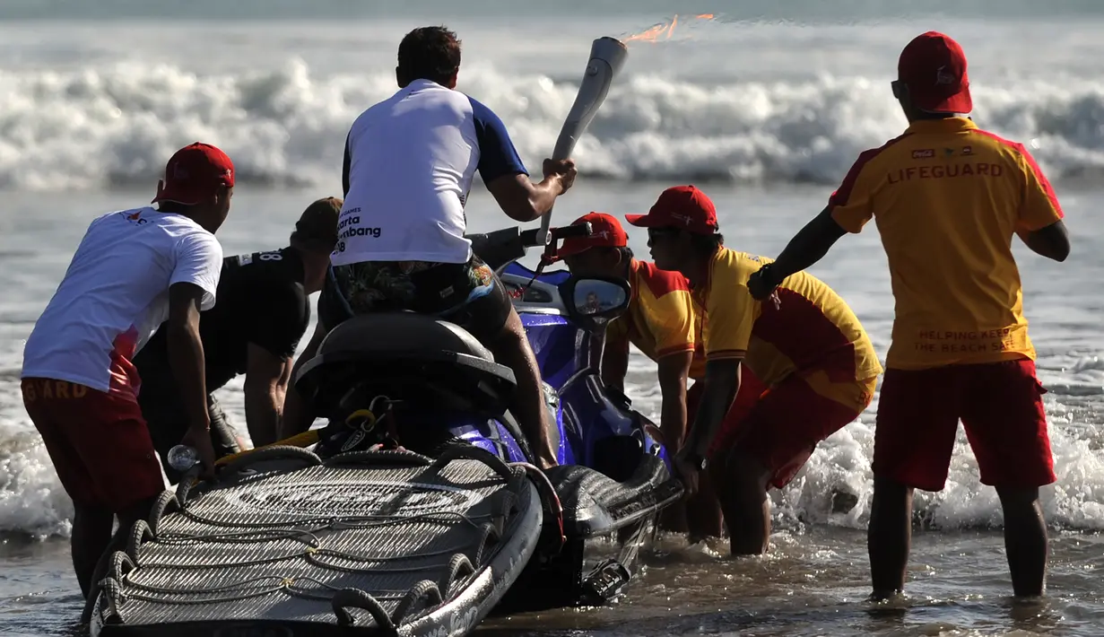 Aktor Hamish Daud bersiap berselancar ke tengah laut  sambil membawa obor Asian Games 2018 di Pantai Kuta, Bali, Senin (23/7). Api obor Asian Games sempat padam saat Hamish Daud membawa obor sambil berselancar di Pantai Kuta. (AFP/SONNY TUMBELAKA)