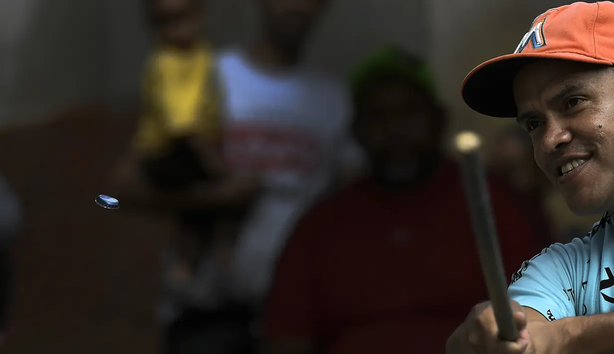 Seorang pemukul mengayunkan tutup botol saat memainkan permainan tradisional "chapitas" atau Caps, di Caracas, Venezuela, 29 Januari 2022. Permainan populer mirip dengan bisbol ini dimainkan dengan tutup botol sebagai pengganti bola, dan tongkat sebagai pengganti pemukul. (AP/Matias Delacroix)