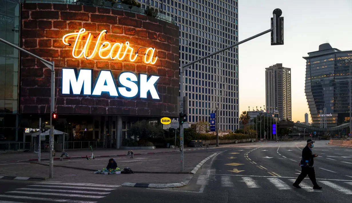 Seorang pria menyeberang jalan di samping papan reklame yang menyerukan agar orang-orang memakai masker selama lockdown nasional menyusul langkah-langkah pemerintah untuk membantu menghentikan penyebaran virus corona COVID-19 di Tel Aviv, Israel, Jumat (8/1/2021). (AP Photo/Oded Balilty)