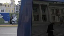 Pejalan kaki tercermin di jendela kendaraan di pelabuhan Piraeus, dekat Athena, Senin (13/12/2021). Yunani meningkatkan kampanye vaksinasi menjelang liburan Natal saat negara itu bergulat dengan lonjakan infeksi yang membawa angka kematian COVID-19 mendekati rekor. (AP/Thanassis Stavrakis)