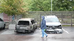 Pejalan kaki melintasi mobil yang hangus terbakar oleh orang tak dikenal di kota Gothenburg, Swedia, Selasa (14/8). Aksi vandalisme besar-besaran ini juga terjadi menjelang pemilu yang digelar pada 9 September ini. (Henrik BRUNNSGARD/TT News Agency/AFP)