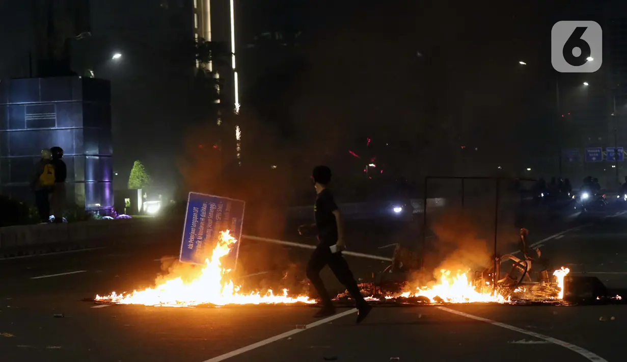 Seorang pemuda melintasi sisa pembakaran di Jalan Jenderal Sudirman, Jakarta, Kamis (8/10/2020). Unjuk rasa menentang disahkannya Omnibus Law UU Cipta Kerja berujung aksi anarkis merusak berbagai fasilitas umum. (Liputan6.com/Helmi Fithriansyah)