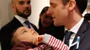 Presiden Prancis Emmanuel Macron menggendong seorang anak saat mengunjungi Graffiti's- Association Le Moulin Vert di Normandia, Prancis (5/4). Pada kunjungannya Presiden Emmanuel Macron berinteraksi dengan anak-anak autis.  (AP / Christophe Ena, Pool)