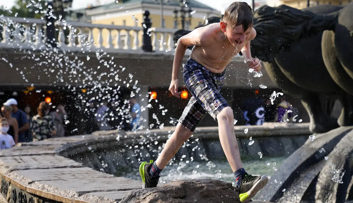 Seorang anak laki-laki mendinginkan dirinya dengan berlari melalui air mancur di Lapangan Manezhnaya dekat Lapangan Merah, Moskow, Rusia, Jumat (25/6/2021). Suhu tengah hari di Moskow mencapai 33 Celcius (91,4 Fahrenheit). (AP Photo/Alexander Zemlianichenko)