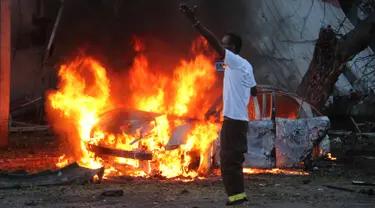 Seorang pria berdiri di dekat sebuah mobil yang terbakar setelah sebuah serangan bom di sebuah restoran di Mogadishu, Somalia (8/5). Setidaknya 6 orang tewas dan 10 orang lainnya terluka dalam serangan bom mobil tersebut. (AP Photo/Farah Abdi Warsameh)