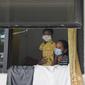Pasien Covid-19 bersama seorang anak terlihat dari jendela Graha Wisata Ragunan, Jakarta, Selasa (15/6/2021). Pemprov DKI memfungsikan kembali Graha Wisata Ragunan sebagai tempat isolasi warga terpapar COVID-19 kategori OTG sejak pekan lalu dan saat ini merawat 117 pasien. (merdeka.com/Arie Basuki)