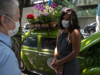 Roberta Machado (kanan) asal Brasil dan pelanggan berbincang di sebelah VW Beetle 1969 miliknya yang diubah menjadi toko bunga keliling di Copacabana, Rio de Janeiro, Rabu (14/10/2020). Perempuan 51 tahun ini mengubah VW kodok untuk bertahan dari krisis akibat pandemi COVID-19. (MAURO PIMENTEL/AFP)