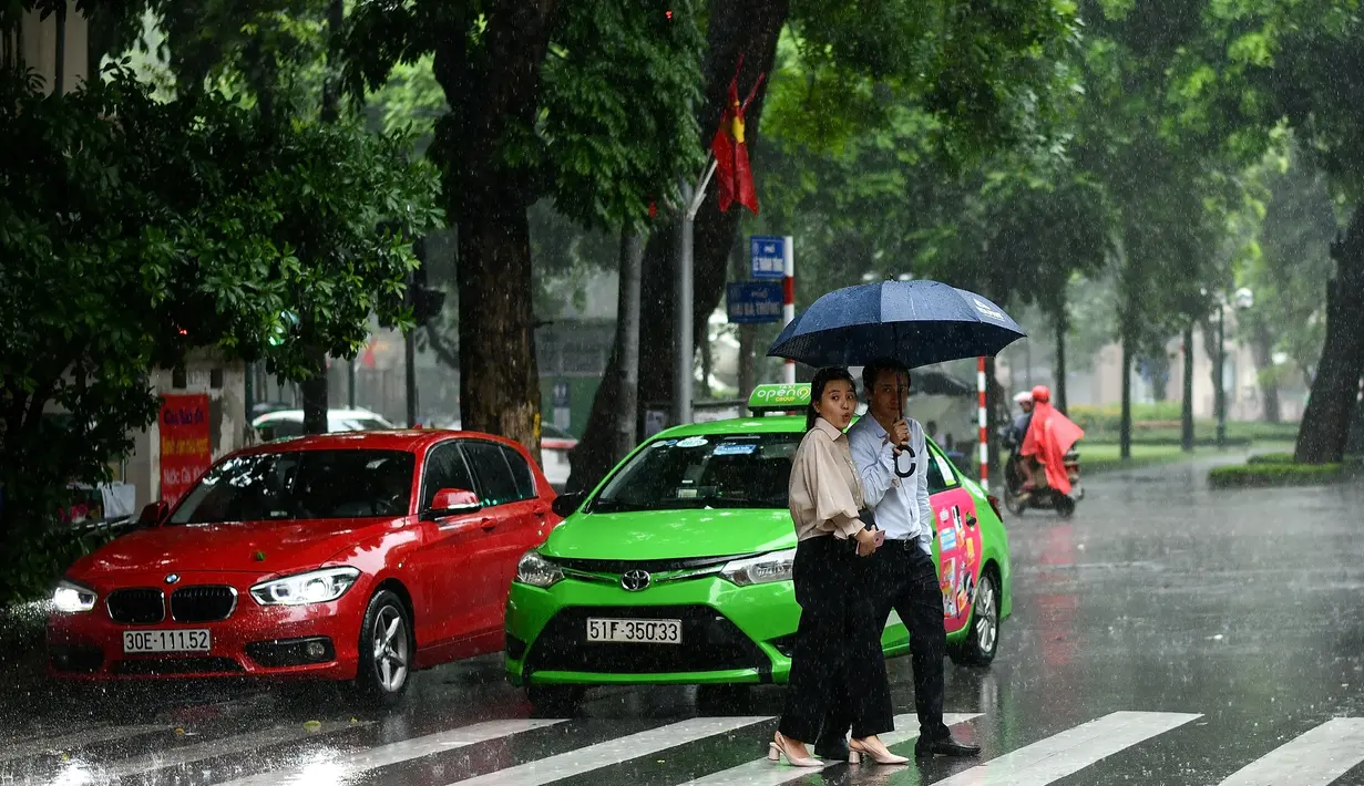 Pejalan kaki menyeberang jalan saat hujan deras di Hanoi (14/10/2020). Badai tropis Nangka menghantam Vietnam tengah-utara yang mengakibatkan bencana alam, terutama hujan lebat dan banjir, telah menyebabkan 28 orang tewas dan 12 lainnya hilang. (AFP Photo/Manan Vatsyayana)