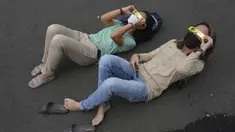 Orang-orang berbaring di tanah saat mereka menggunakan kacamata khusus untuk menyaksikan gerhana matahari hibrida di Jakarta, Kamis (20/4/2023). (AP Photo/Tatan Syuflana)