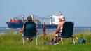 Warga berjemur ketika kapal kargo menuju Laut Utara saat suhu mencapai 34 derajat Celcius di dekat pantai Laut Utara di Wremen, Jerman barat (24/7/2019). (AFP Photo/Patrik Stollarz)