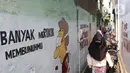 Warga melintasi mural bertema kawasan bebas asap rokok di lingkungan RW 06 Kelurahan Kayu Manis, Matraman, Jakarta, Jumat (8/10/2021). Warga sejumlah RT di RW 06 berkomitmen menjaga lingkungan dari asap rokok dengan memberikan teguran dan sanksi bagi yang melanggar. (Liputan6.com/Herman Zakharia)