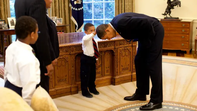 Presiden Obama ketika membiarkan anak seorang pegawai Gedung Putih menyentuh kepalanya. (Sumber Wikimedia Commons)