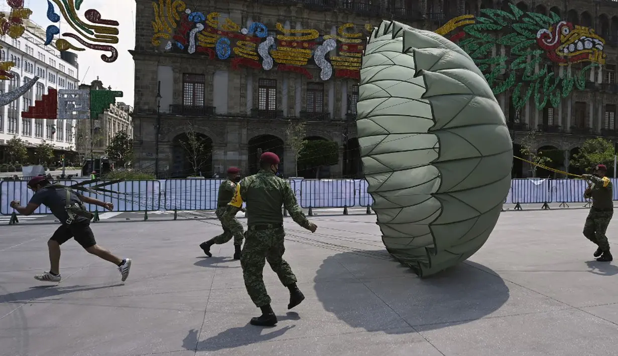 Pasukan terjun payung membantu seorang pria berlari dengan parasut terbuka dalam pameran yang disebut The Great Force of Mexico di Alun-Alun Zocalo, Mexico City, Meksiko, 20 September 2021. (ALFREDO ESTRELLA/AFP)