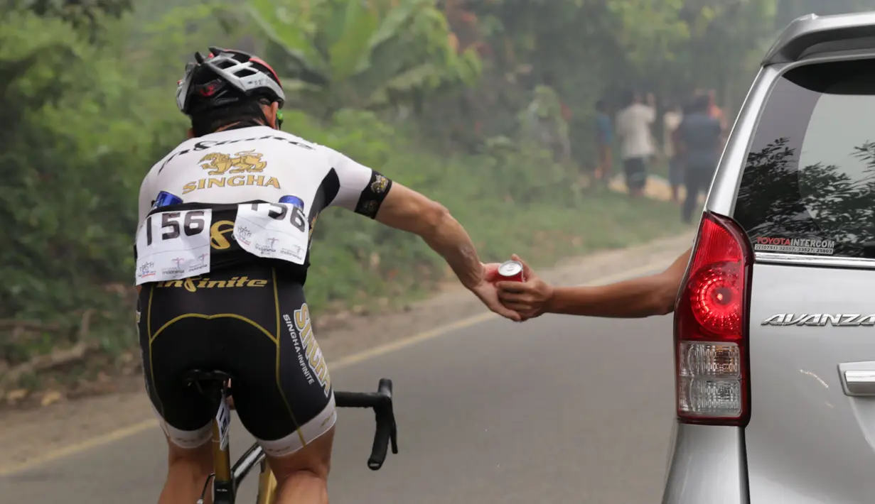 Seorang pebalap Singha Infinitife Team mengambil suplai makanan dan minuman dari mobil pendukung dalam Etape 3 Tour de Singkarak 2015 antara Sijunjung menuju Dharmasraya, Sumatra Barat, Senin (5/10/2015). (Bola.com/Arief Bagus)