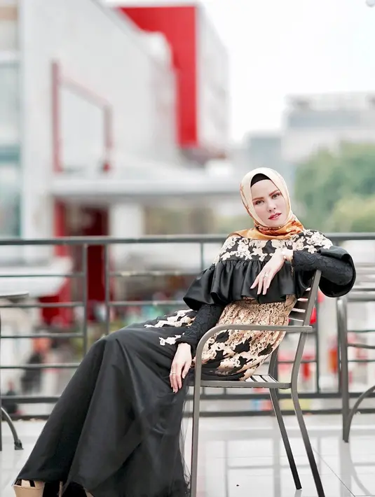 Coba lihat, outfit yang dipakai Angel ini cukup glamor bukan? Long dress hitam dengan motif bunga-bunga ini juga terdapat aksen rempel di bagian dadanya. Makin terlihat mewah dengan hijab berwarna oranye. (Instagram/angellelga)