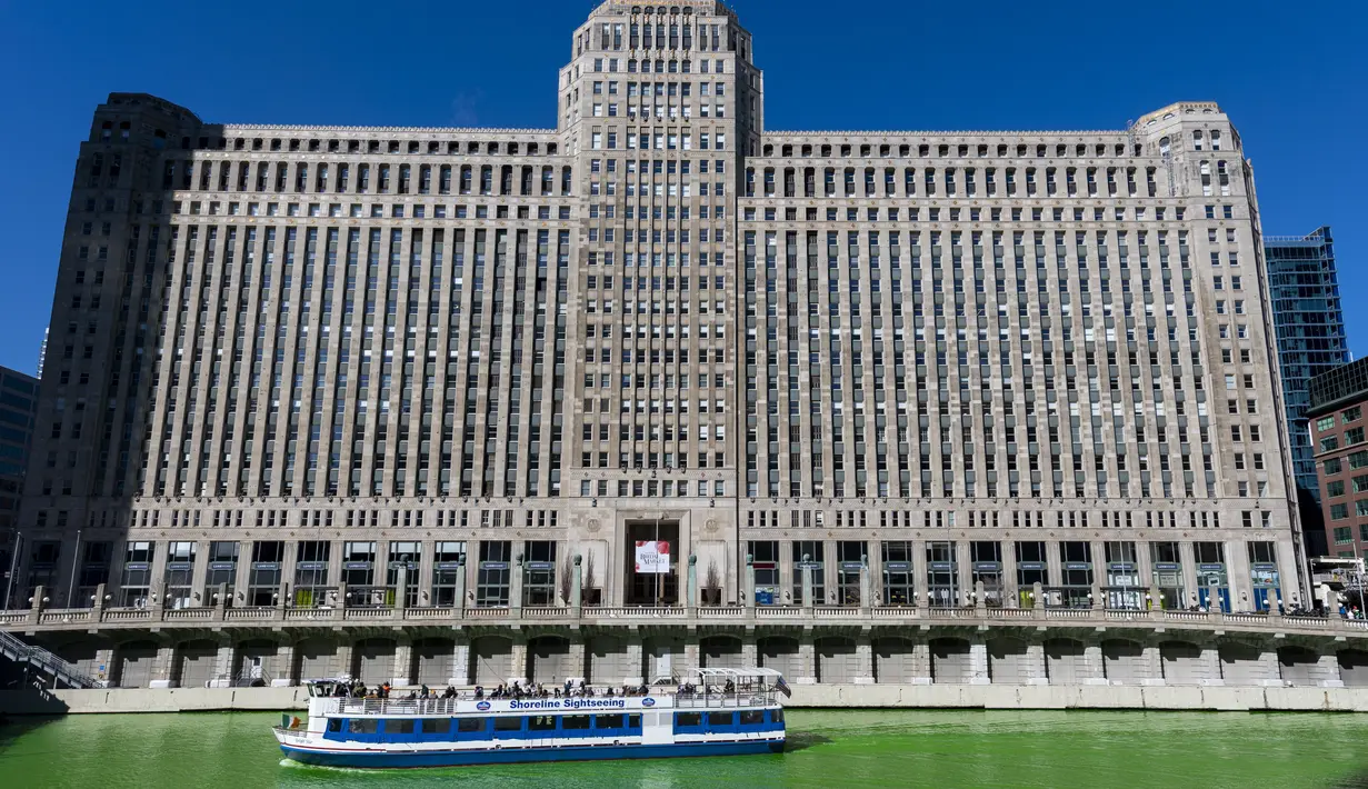Kapal wisata Chicago Shoreline Sightseeing melewati Merchandise Mart saat Sungai Chicago diwarnai hijau, Sabtu (12/3/2022). Perubahan warna ini dilakukan untuk menyambut Hari St. Patrick pada Kamis mendatang. (Tyler Pasciak LaRiviere/Chicago Sun-Times via AP)