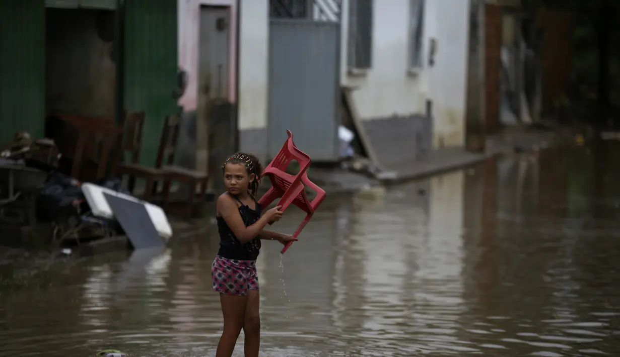 Seorang gadis membawa kursi saat banjir di Itapetinga, negara bagian Bahia, Brasil, Selasa (28/12/2021). Dua bendungan jebol pada Minggu (26/12) di timur laut Brasil, mengancam banjir yang lebih parah di wilayah yang diguyur hujan. (AP/Raphael Muller)