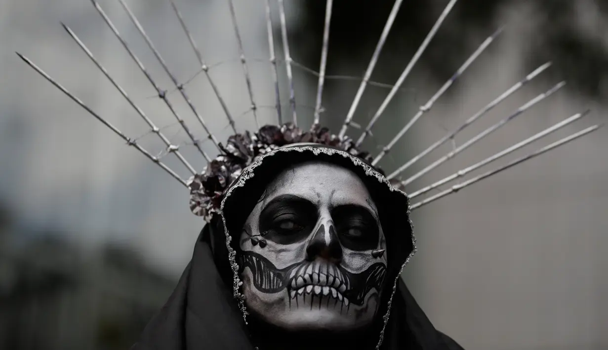 Seorang wanita mengenakan kostum tengkorak menunggu dimulainya Prosesi Grand Catrinas, untuk menandai perayaan Day of The Dead, di Mexico City, Minggu (22/10). Dalam prosesi tersebut warga berdandan menyerupai kerangka. (AP/Rebecca Blackwell)