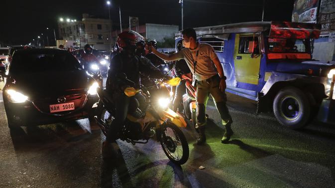 Petugas lalu lintas memeriksa suhu tubuh pengendara sepeda motor di pos pemeriksaan virus corona COVID-19 di Manila, Filipina, Senin (16/3/2020). Polisi beserta petugas lalu lintas dan petugas desa mengecek suhu tubuh warga untuk mencegah penyebaran virus corona COVID-19. (AP Photo/Aaron Favila)