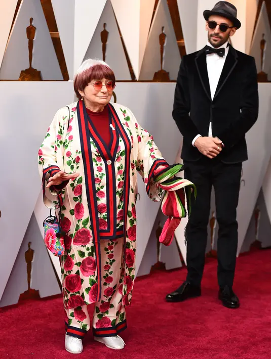 Agnes Varda dan JR menghadiri malam penghargaan Piala Oscar 2018, Los Angeles, Minggu (4/3). Sutrada Prancis itu memadukan kardigan sutra Gucci motif bunga, celana dan kimono lengkap dengan kacamata bulat khas John Lennon. (Jordan Strauss/Invision/AP)