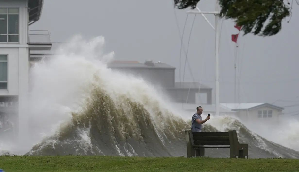 Seorang pria mengambil gambar gelombang tinggi di sepanjang tepi Danau Pontchartrain saat Badai Ida mendekat di New Orleans, Minggu (29/8/2021). Di salah satu kota terbesar Louisiana, New Orleans, otoritas kesehatan menangguhkan layanan medis darurat. (AP Photo/Eric Gay)