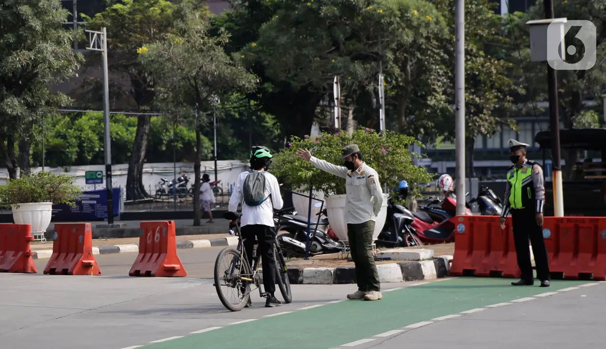 Petugas gabungan mengarahkan pengguna sepeda saat pengalihan jalur pesepeda di kawasan Sudirman-Thamrin, Jakarta, Minggu (5/9/2021). Pemberlakuan jalur ganjil genap pada masa PPKM membuat pengguna sepeda dilarang melintasi kawasan ganjil-genap pagi ini. (Liputan6.com/Angga Yuniar)