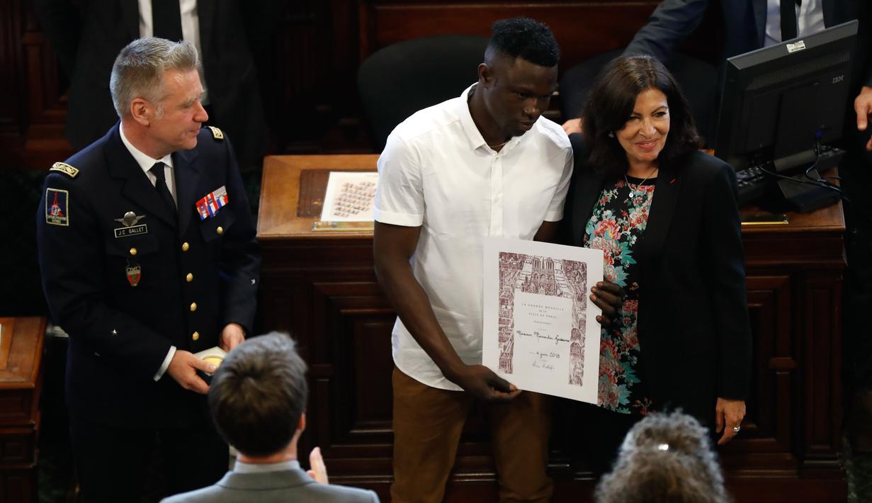 Imigran Mali Mamoudou Gassama dianugerahi medali Grand Vermeil oleh walikota Paris Anne Hidalgo (kanan) di Paris, Prancis (4/6). Sebelumnya Mamoudou dijuluki "Spider-Man" karena menyelamatkan balita yang nyaris jatuh dari apartemen. (AFP/Francois Guillot)