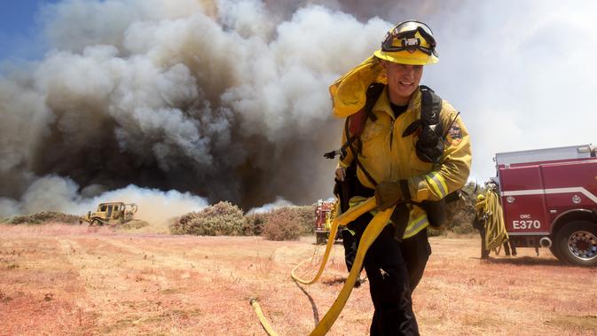Petugas pemadam kebakaran berusaha memadamkan api di Cherry Valley, California (1/8/2020). Kebakaran lahan juga telah menjalar ke rumah penduduk. (AP Photo/Ringo H.W. Chiu)