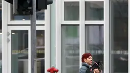 Seorang ibu menunggu di perempatan jalan untuk menyeberang dengan lampu lalu lintas khusus pejalan kaki yang menampilkan simbol wanita di Vilnius, Lituania, Jumat (2/11). (Petras Malukas/AFP)