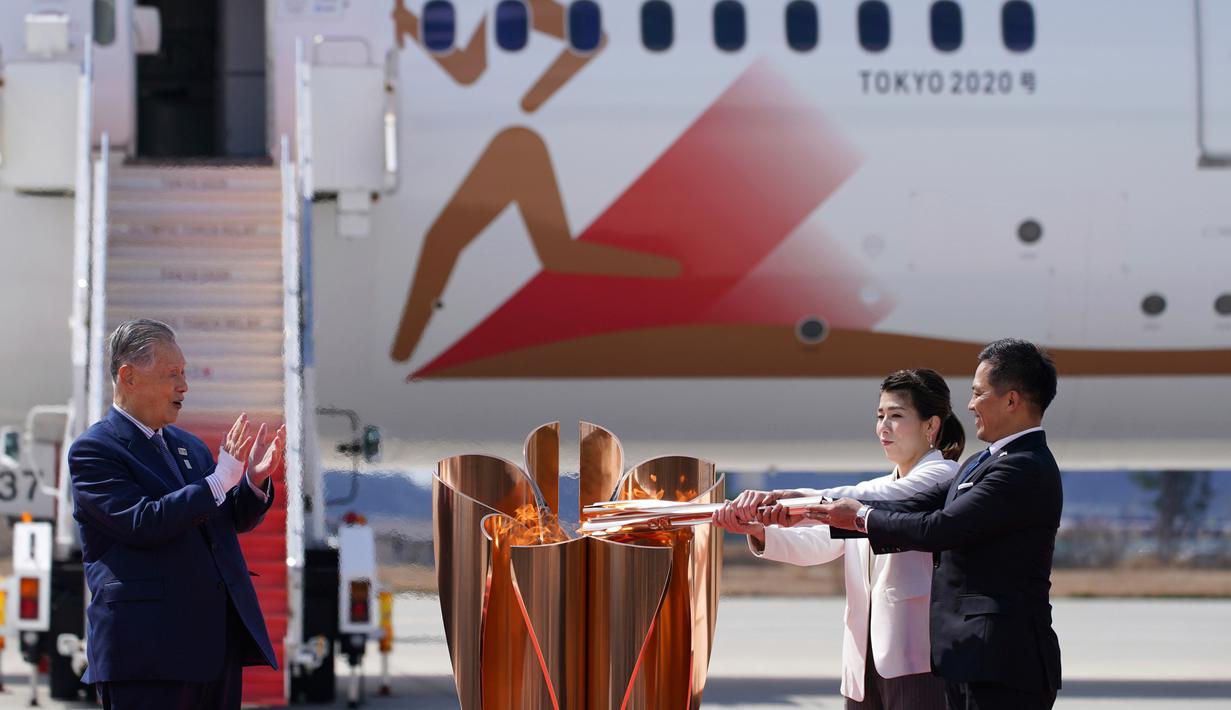 Presiden Olimpiade Tokyo 2020 Yoshiro Mori (kiri) menyaksikan dua atlet peraih tiga kali medali emas olimpiade Tadahiro Nomura (kanan) dan Saori Yoshida menyalakan obor Olimpiade saat tiba dari Yunani di Pangkalan Udara Matsushima, Prefektur Miyagi, Jepang, Jumat (20/3/2020).  (AP/Eugene Hoshiko)