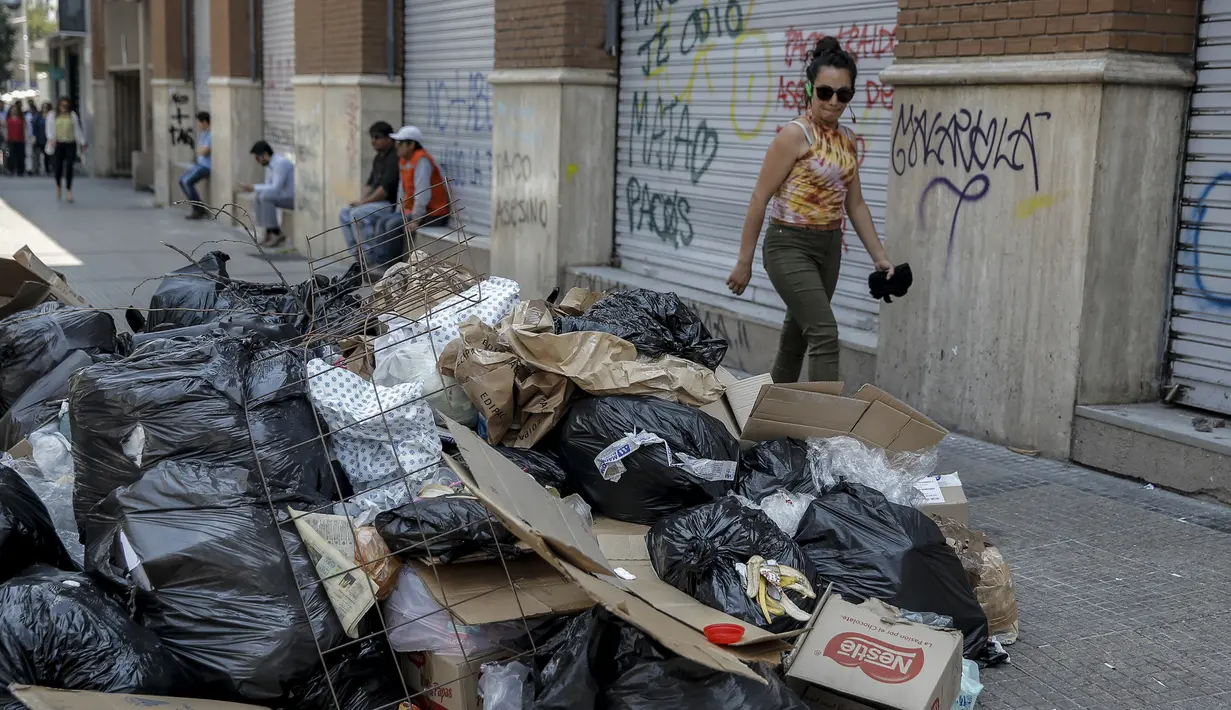 Seorang wanita berjalan melewati tumpukan sampah akibat pemogokan petugas sampah di Santiago (14/11/2019). Protes kekerasan meletus di ibukota Chile, Santiago, pada Selasa ketika mata uang negara itu turun ke level terendah dalam sejarah. (AFP/Javier Torres)