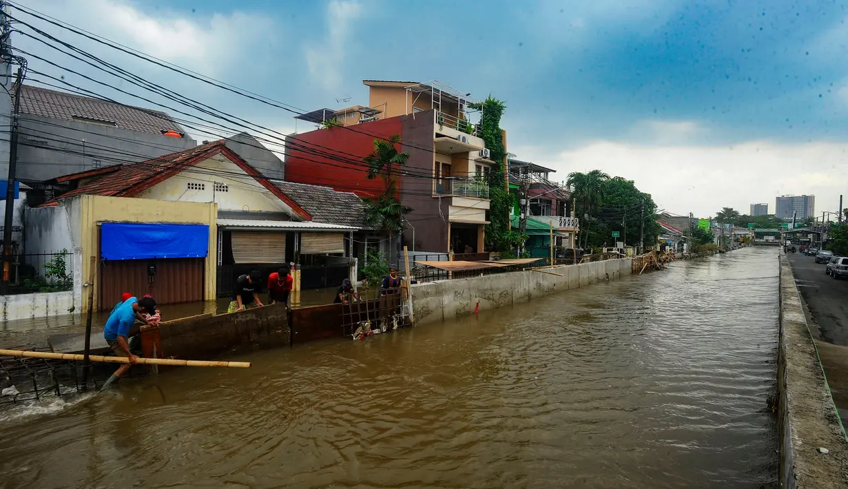 Pekerja membuat penahan tanggul kali sementara sepanjang 20 meter menggunakan papan, karung berisi pasir, dan rangka besi cor untuk mengurangi debit air yang masuk ke pemukiman warga. (merdeka.com/Arie Basuki)