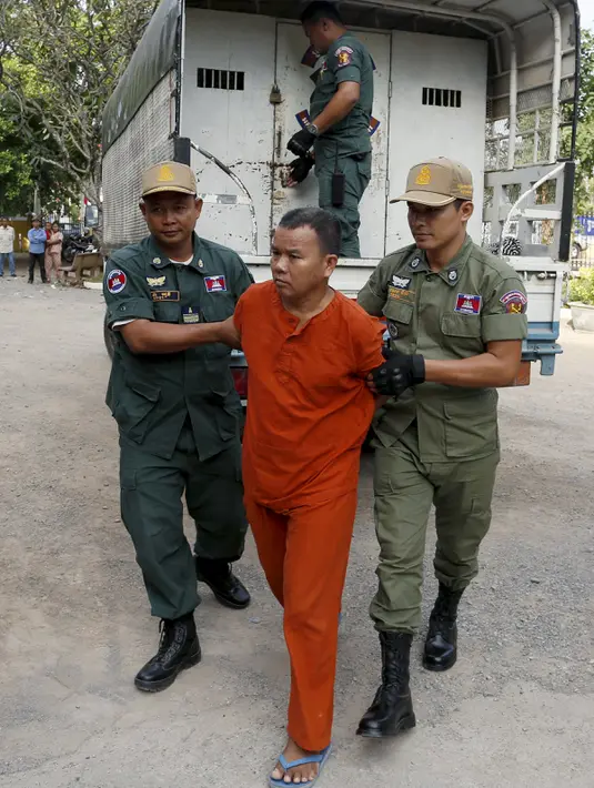 Yem Chrin (tengah) dikawal oleh petugas polisi saat tiba di Pengadilan Provinsi Battambang,Kamboja,Kamis (3/12). Diduga dalam prakteknya Yem Chrin menggunakan obat tak berlisensi, suntik bekas dan melakukan malpraktek. (REUTERS/Stringer)
