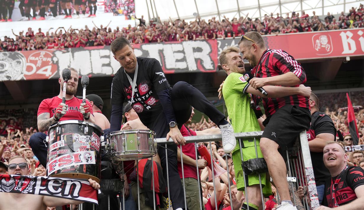 Pelatih Bayer Leverkusen, Xabi Alonso, memanjat tribun penonton saat merayakan gelar juara Bundesliga 2024 bersama suporter di BayArena, Sabtu (18/5/2024). (AP Photo/Martin Meissner)